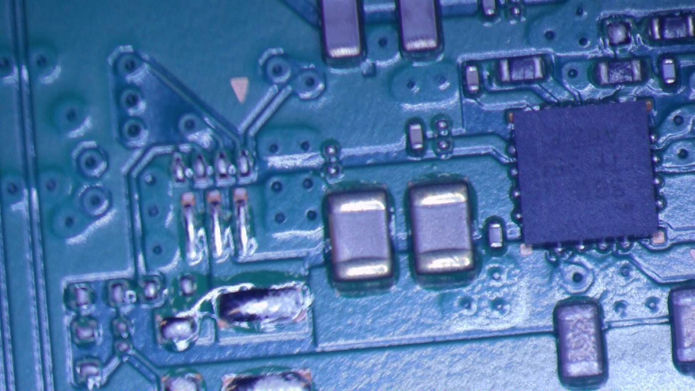 Prasknutý SMD kondenzátor na doske PlayStation 5 pod mikroskopom – konzola len pípla, bez obrazu a svetla